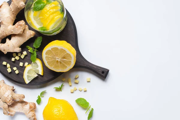 Vue de dessus de la limonade fraîche en verre près de citrons et racine de gingembre sur panneau en bois noir sur fond blanc — Photo de stock