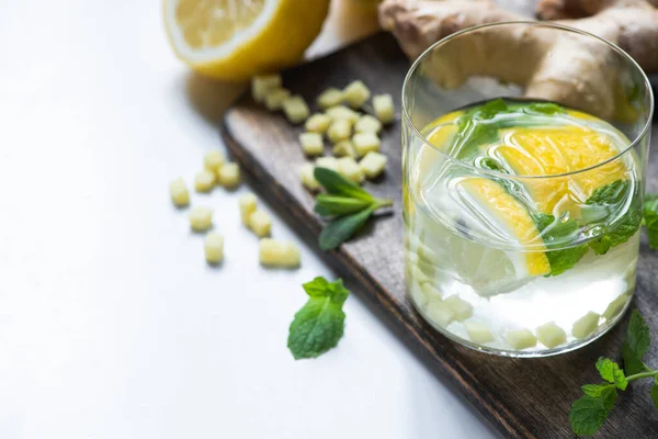 Selective focus of fresh ginger lemonade in glass with lemon and mint on wooden board on white background — Stock Photo