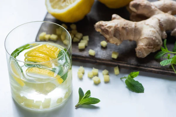 Selective focus of fresh ginger lemonade in glass with lemon and mint on wooden board on white background — Stock Photo