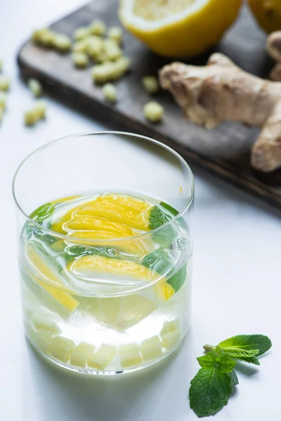 Selective focus of fresh ginger lemonade in glass with lemon and mint on wooden board on white background — Stock Photo