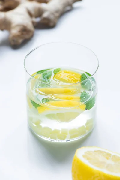Селективний фокус свіжого лимонаду в склянці біля кореня лимона та імбиру на білому фоні — стокове фото