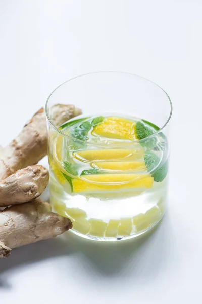 Limonada fresca en vaso con limón cerca de raíz de jengibre sobre fondo blanco - foto de stock