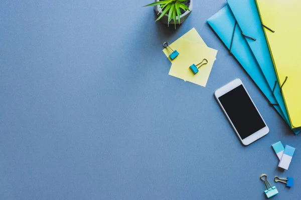 Vue du dessus du smartphone près de la papeterie et de la plante sur la surface bleue — Photo de stock