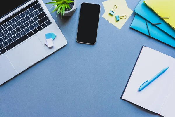 Vista superior do smartphone, laptop e artigos de papelaria em fundo azul — Fotografia de Stock