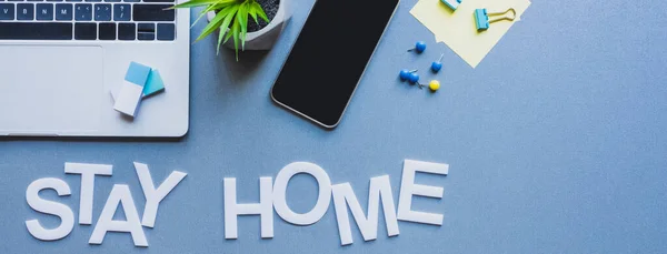 Récolte panoramique de gadgets, papeterie et plantes près de rester lettrage à la maison sur la surface bleue — Photo de stock