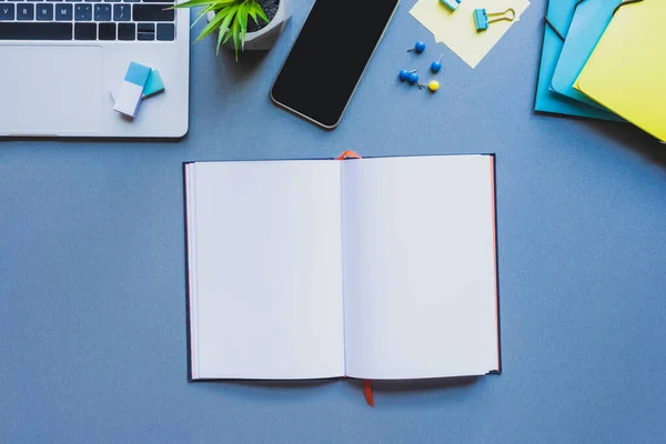 Vue du dessus du bloc-notes ouvert près des appareils numériques et des fournitures de bureau sur la surface bleue — Photo de stock