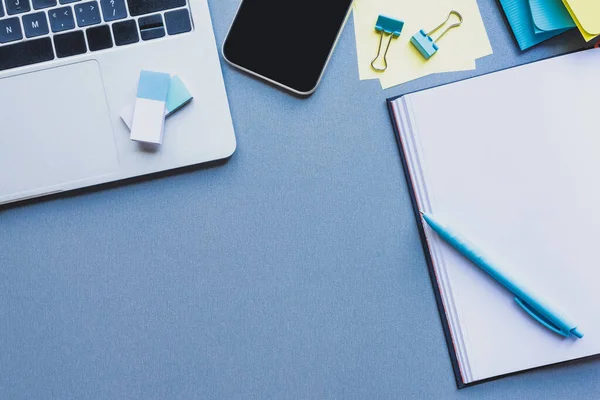 Top view of digital devices, stationery and open notebook on blue surface — Stock Photo