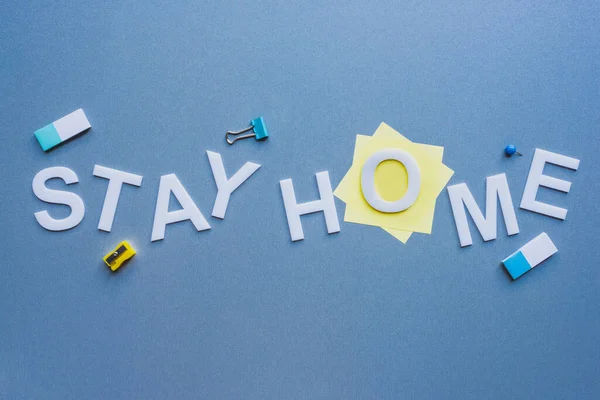 Top view of stay home lettering near stationery on blue surface — Stock Photo