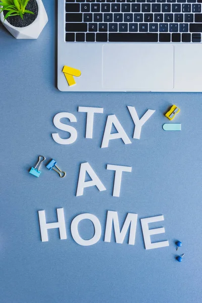 Vista superior de la estancia en casa con letras cerca de la computadora portátil, la planta y los artículos de papelería sobre fondo azul - foto de stock