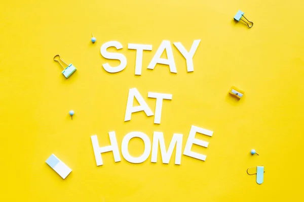 Top view of stay at home lettering near binder clips and pencil sharpener on yellow surface — Stock Photo