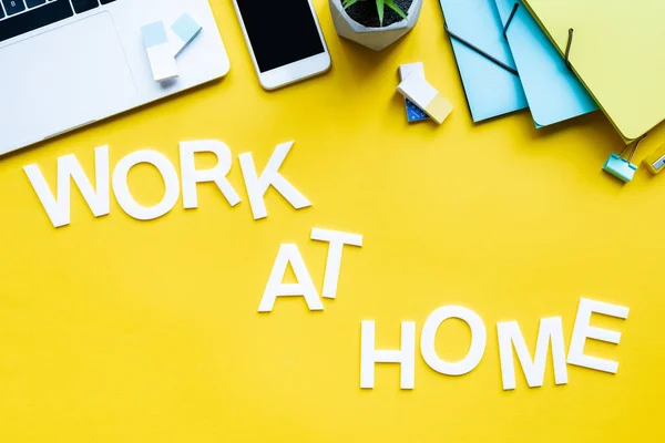 Vista superior del trabajo en casa con letras cerca de gadgets y papelería en la superficie amarilla - foto de stock