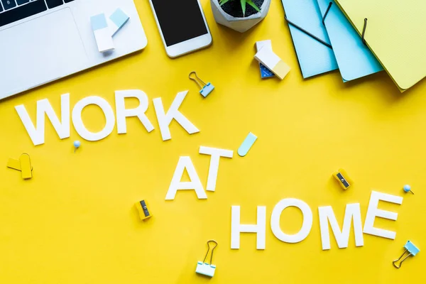 Vista superior del trabajo en casa con letras cerca de teléfonos inteligentes, portátiles y suministros de oficina en la superficie amarilla - foto de stock