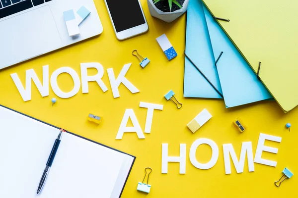 Top view of work at home lettering near open notebook and stationery on yellow background — Stock Photo