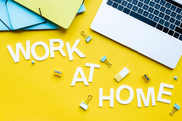 Vista superior del trabajo en casa con letras cerca de la computadora portátil y artículos de papelería sobre fondo amarillo - foto de stock