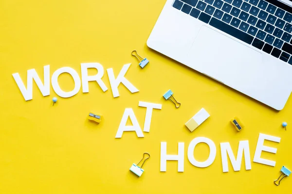 Top view of work at home lettering near laptop, binder clips and pencil sharpeners on yellow surface — Stock Photo