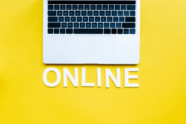 Top view of laptop and online lettering on yellow surface — Stock Photo