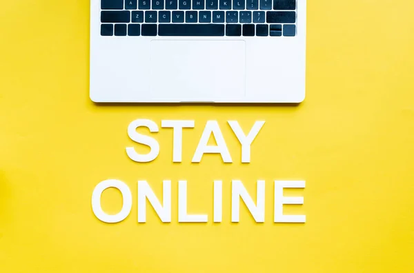 Top view of stay online lettering and laptop on yellow surface — Stock Photo