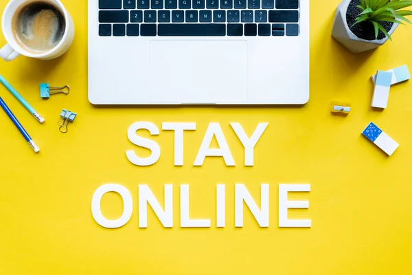 Top view of stay online lettering near laptop, coffee and stationery on yellow background — Stock Photo