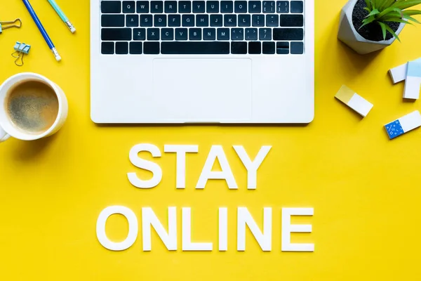 Vista superior de lettering ficar online perto de laptop, xícara de café e material de escritório na superfície amarela — Fotografia de Stock