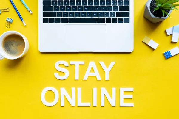 Top view of lettering stay online near laptop, cup of coffee and office supplies on yellow surface — Stock Photo