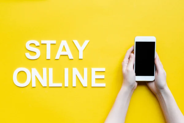 Top view of woman holding smartphone near stay online lettering on yellow background — Stock Photo
