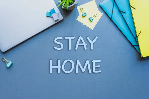 Vista superior de ficar em casa lettering perto de laptop, planta e papelaria na superfície azul — Fotografia de Stock