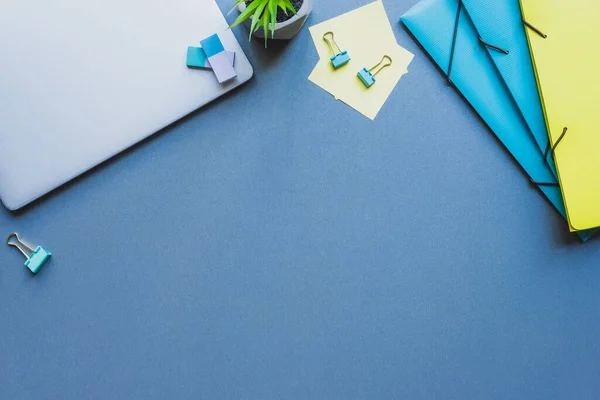 Vue du dessus de l'ordinateur portable, des dossiers en papier et de la papeterie sur fond bleu — Photo de stock