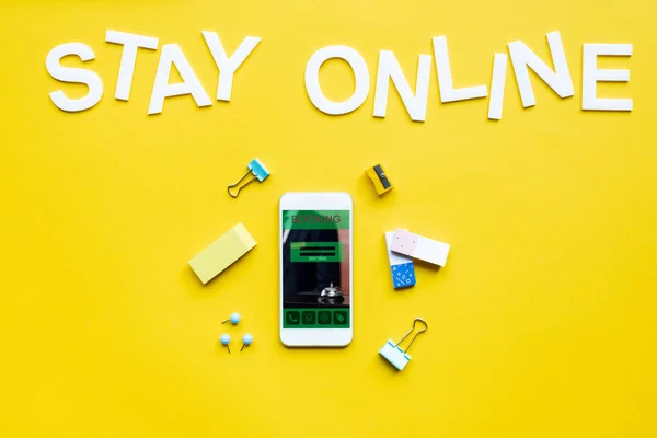 Top view of stay online lettering near smartphone with booking app on yellow surface — Stock Photo