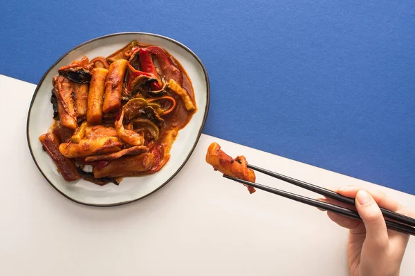 Top view of woman holding chopsticks with korean topokki on white and blue — Stock Photo