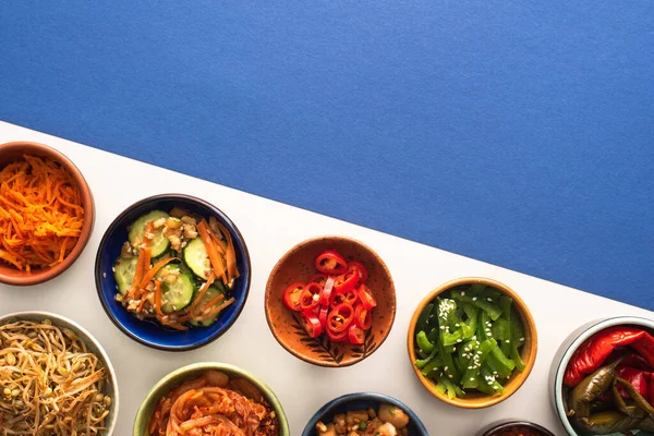 Vue de dessus des bols avec des plats d'accompagnement traditionnels coréens sur bleu et blanc — Photo de stock