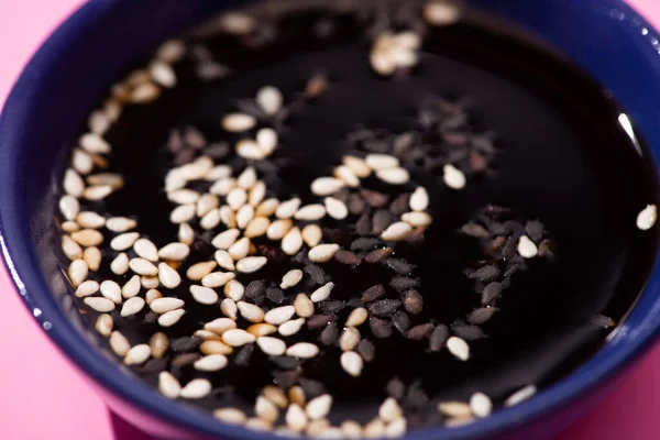 Close up of soy sauce with sesame in bowl on pink — Stock Photo