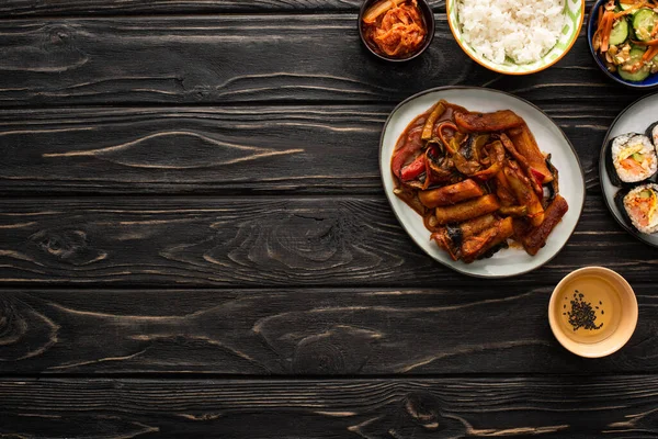 Top view of korean kimchi, kimbap and topokki near rice and sesame oil on wooden surface — Stock Photo