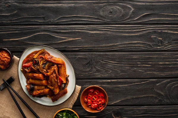 Top view of korean topokki near chopsticks, side dishes and cotton napkin on wooden surface — Stock Photo