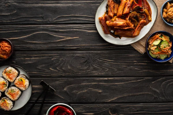 Top view of korean topokki near traditional side dishes, chopsticks and cotton napkin on wooden surface — Stock Photo