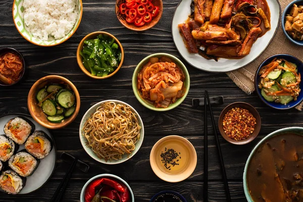 Верхний вид корейских традиционных блюд возле палочек для еды и хлопковой салфетки на деревянной поверхности — стоковое фото