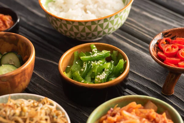 Foyer sélectif de sésame sur les poivrons verts près du riz et des plats d'accompagnement coréens sur la surface en bois — Photo de stock