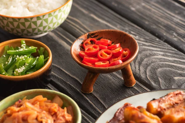Selective focus of green bell peppers near rice, spicy chili peppers and korean side dishes on wooden surface — Stock Photo