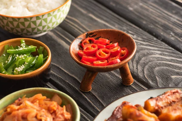 Selektiver Fokus grüner Paprika in der Nähe von Reis, würzigen Chilischoten und koreanischen Beilagen auf Holzoberfläche — Stockfoto