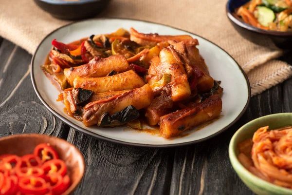 Selective focus of spicy topokki near red chili peppers on wooden surface — Stock Photo