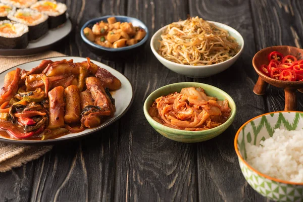 Selective focus of traditional topokki near tasty korean dishes on wooden surface — Stock Photo