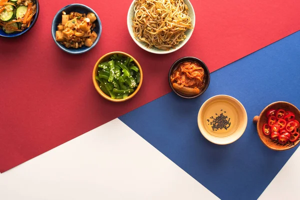 Top view of bowls with korean traditional side dishes and oil on blue, crimson and white — Stock Photo