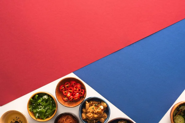 Top view of bowls with korean spicy side dishes and oil on blue, crimson and white — Stock Photo