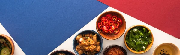 Concept horizontal de bols avec des plats d'accompagnement épicés coréens et de l'huile sur bleu, pourpre et blanc — Photo de stock