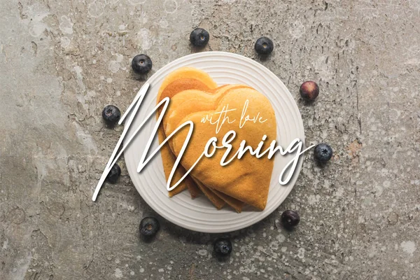 Top view of delicious heart shaped pancakes on plate near blueberries on grey concrete surface, morning illustration — Stock Photo