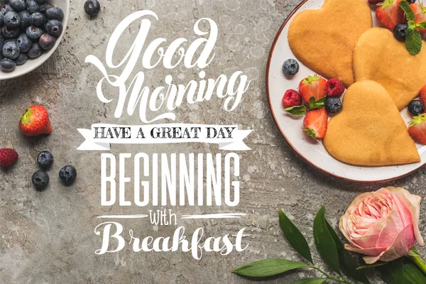 Draufsicht auf herzförmige Pfannkuchen mit Beeren auf grauer Betonoberfläche in der Nähe von Rose, Guten Morgen, guter Start mit Frühstück Illustration — Stockfoto