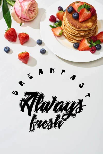 Top view of delicious pancakes with blueberries and strawberries on plate near rose flower on marble white surface, breakfast always fresh illustration — Stock Photo