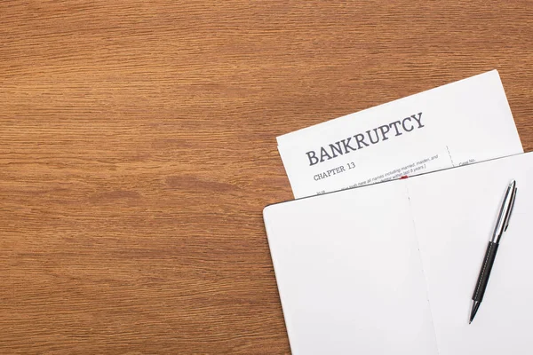Vista superior de papel de falência e notebook em branco com caneta sobre fundo de madeira — Fotografia de Stock