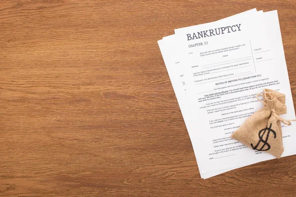 Верхний вид документов о банкротстве и денежный мешок на деревянном фоне — стоковое фото