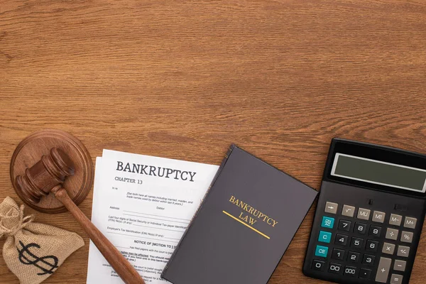 Top view of calculator, bankruptcy law book, documents, money bag and gavel on wooden background — Stock Photo
