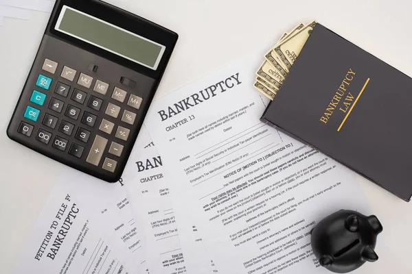 Top view of bankruptcy papers, law book with money, calculator and piggy bank on white background — Stock Photo